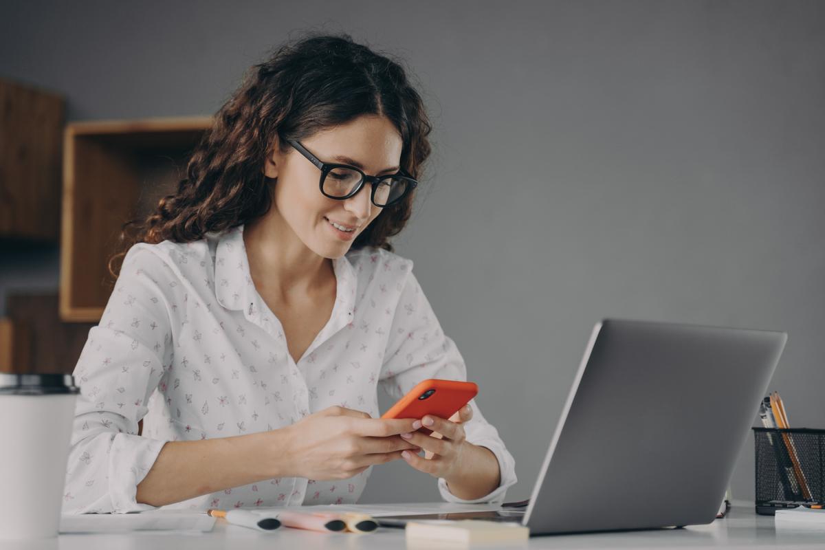 Woman using laptop and looking at mobile phone