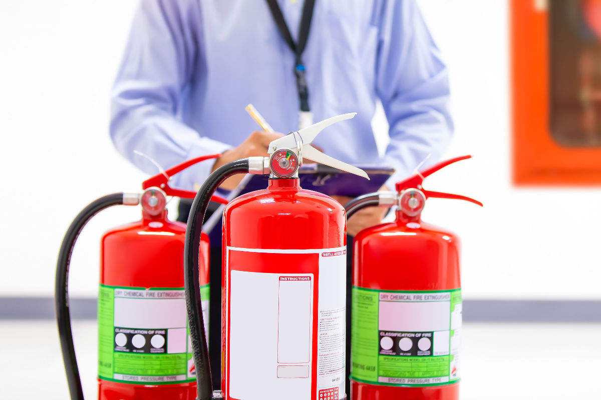 Engineer holding clipboard inspecting pressure gauges on fire extinguishers